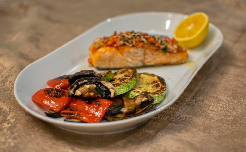 A delicious grilled salmon fillet with roasted vegetables served on a white plate.