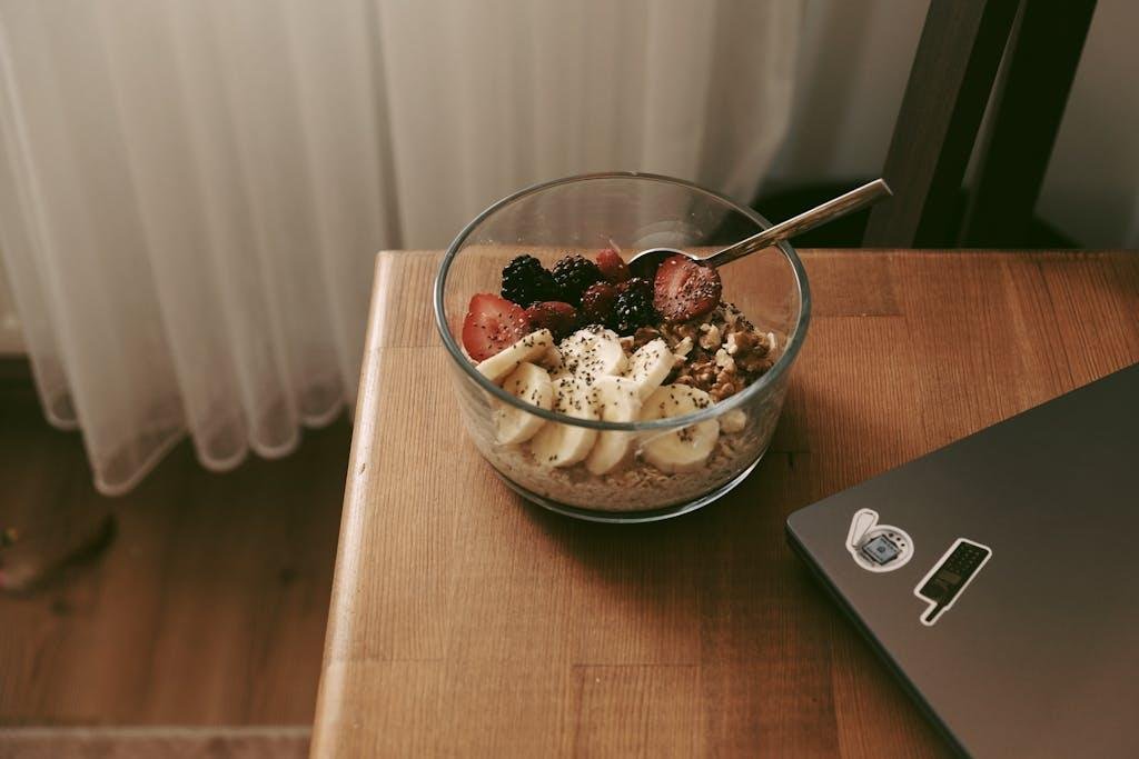 Glass bowl of oats with bananas, strawberries, and nuts on a wooden desk.