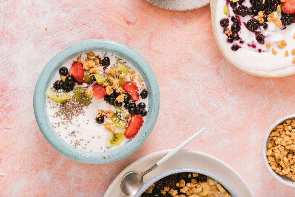 Top view of colorful yogurt bowls topped with fresh berries and granola on a rustic background.