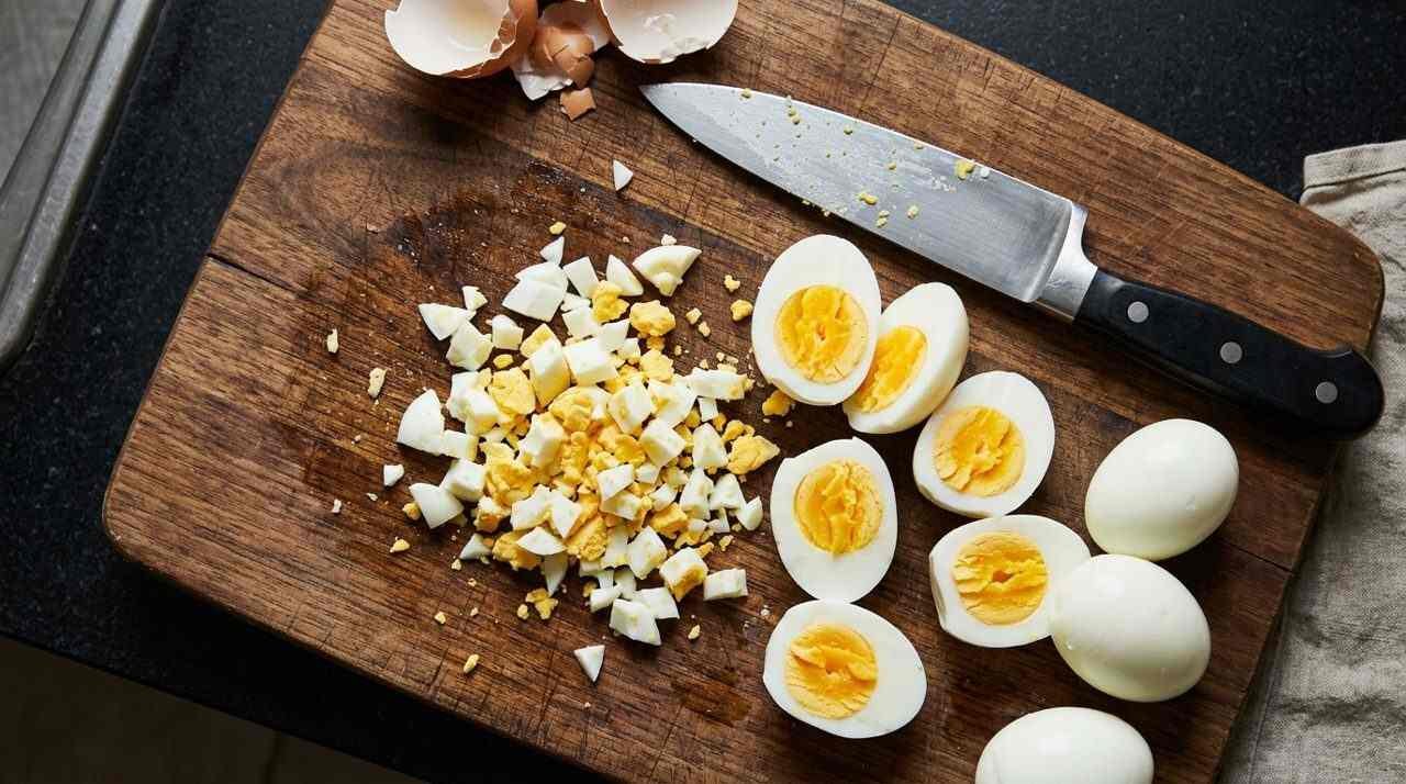 Halved hard-cooked eggs being diced on a wooden board